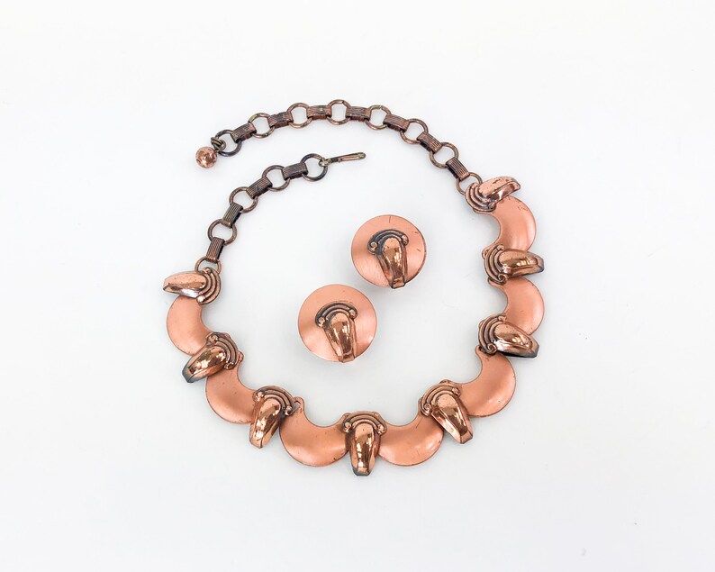 May include: A copper necklace and earrings set with a chain and a series of crescent-shaped pendants with a raised design.