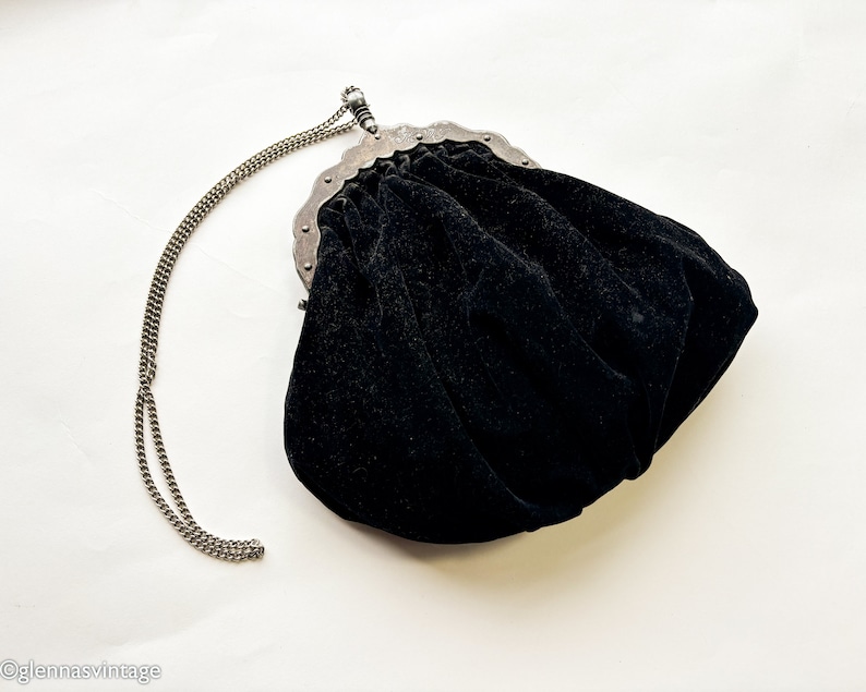 May include: A black velvet evening bag with a silver chain strap and a decorative metal clasp.