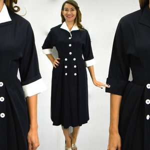 Pode incluir: Um vestido azul marinho com colarinho e punhos brancos. O vestido tem fecho de bot&otilde;es de dupla abotoadura e saia plissada.