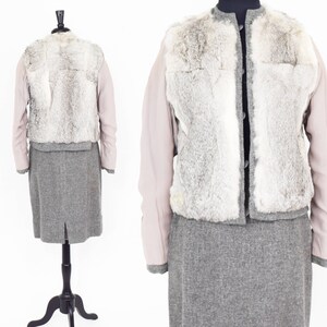 May include: A gray skirt suit with a faux fur vest. The vest has a light gray fur with a white trim. The jacket has long sleeves and a button closure. The skirt is knee-length and has a back slit.