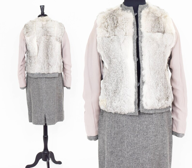 May include: A gray skirt suit with a faux fur vest. The vest has a light gray fur with a white trim. The jacket has long sleeves and a button closure. The skirt is knee-length and has a back slit.