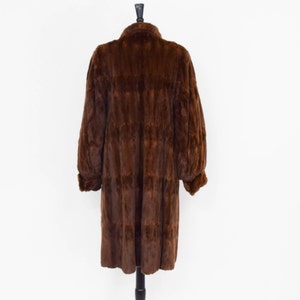 May include: A long brown fur coat with a collar and long sleeves. The coat is on a mannequin and is displayed against a white background.
