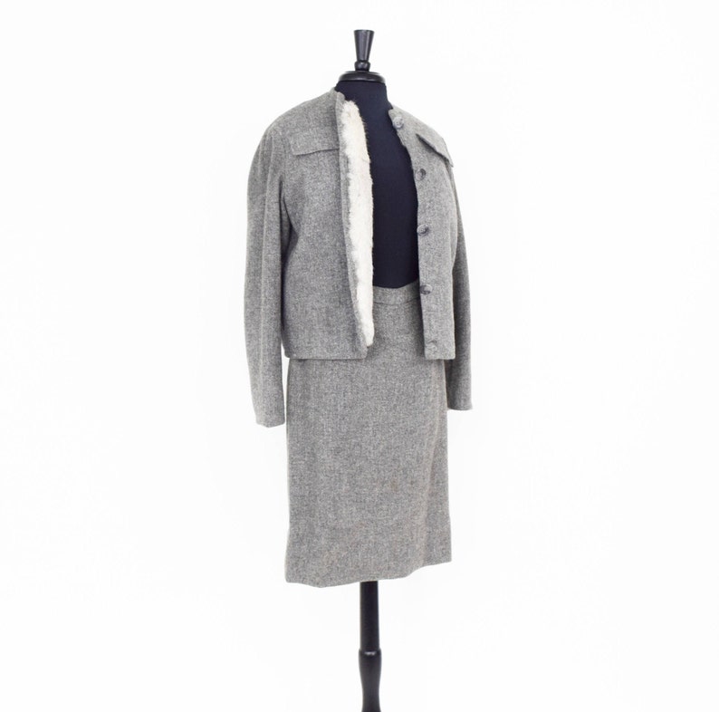May include: A gray tweed skirt suit with a white fur collar on a mannequin.