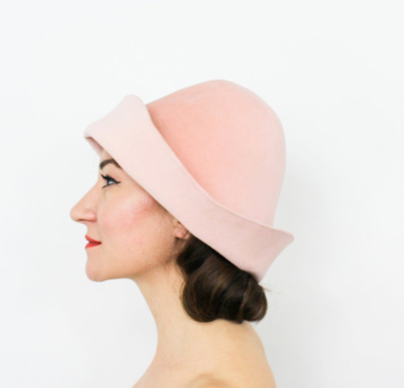 May include: A light pink felt hat with a wide brim and a rounded crown. The hat is tilted slightly to the side.