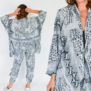 May include: A white and black patterned pantsuit with a long, open-front jacket. The fabric has a snake skin print.