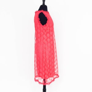 May include: A coral pink sleeveless dress with a floral lace pattern. The dress is on a mannequin and has a scalloped hem.