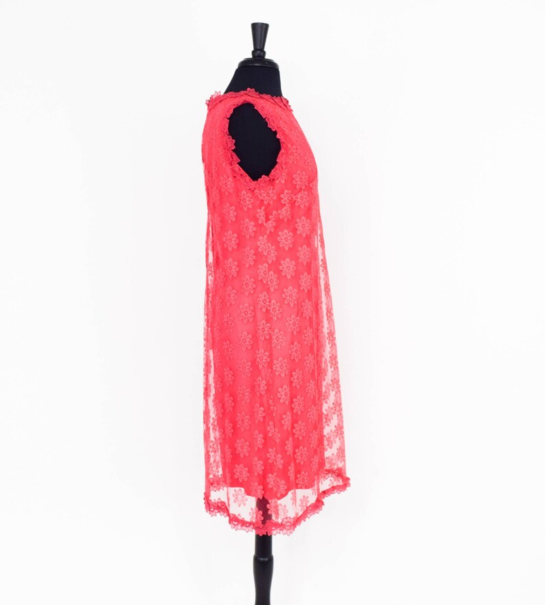 May include: A coral pink sleeveless dress with a floral lace pattern. The dress is on a mannequin and has a scalloped hem.