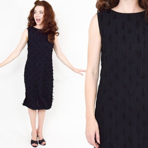 May include: A black sleeveless dress with a textured fringe design. The dress is knee-length and has a scoop neckline.