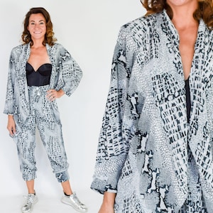 May include: A black and white snake print two-piece outfit. The top is a long-sleeved, open-front jacket. The pants are loose-fitting and cropped.