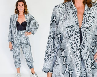 May include: A black and white snake print two-piece outfit. The top is a long-sleeved, open-front jacket. The trousers are loose-fitting and cropped.