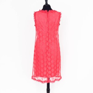 May include: A coral pink sleeveless dress with a floral lace pattern. The dress has a scalloped neckline and hem.