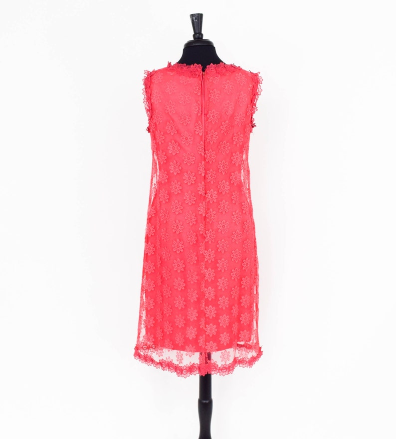 May include: A coral pink sleeveless dress with a floral lace pattern. The dress has a scalloped neckline and hem.