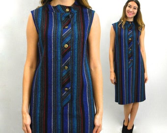 Puede incluir: Vestido sin mangas con rayas verticales en azul, gris y rojo. El vestido presenta un cuello alto y un panel abotonado decorativo en la parte delantera. El vestido, a la altura de la rodilla, tiene una estética vintage.