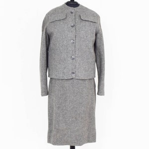 May include: A gray tweed skirt suit with a button-up jacket and a knee-length skirt.