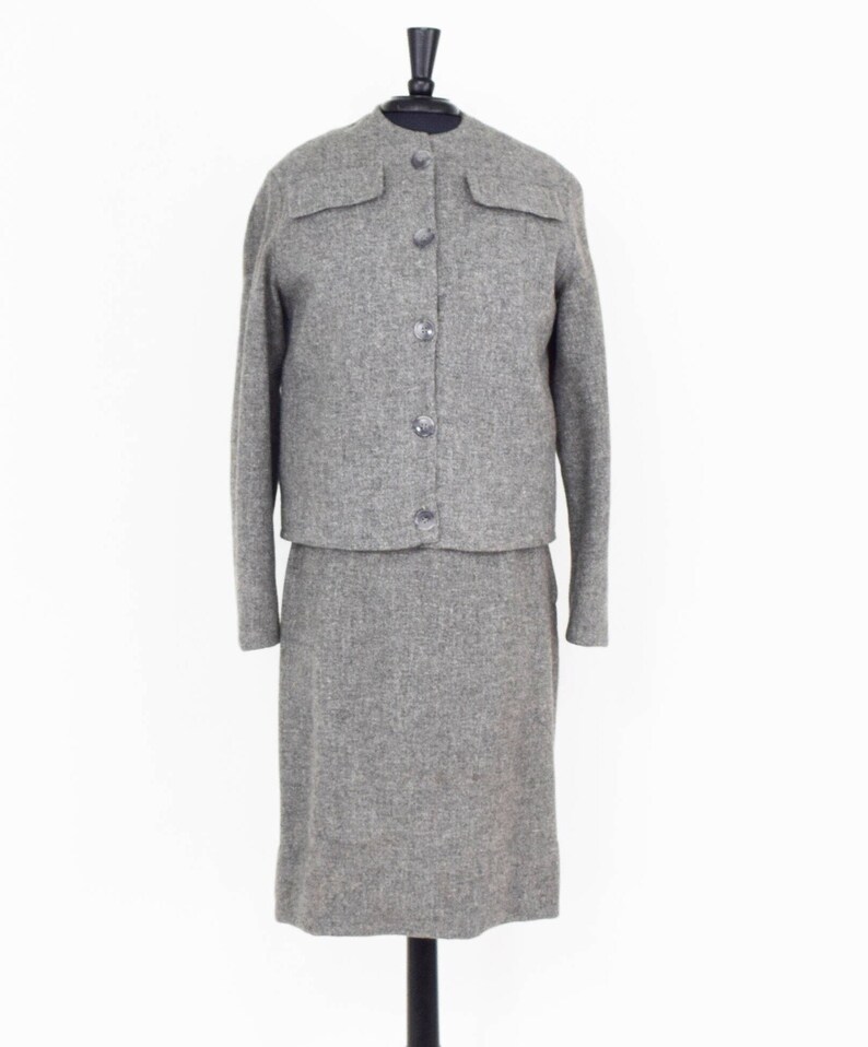 May include: A gray tweed skirt suit with a button-up jacket and a knee-length skirt.