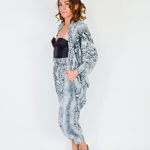 May include: A woman wearing a white and black snake print pantsuit with a black bra. She is wearing silver sneakers and has her hair pulled back.