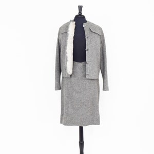 May include: A gray tweed skirt suit with a faux fur collar on the jacket. The jacket has a button closure and the skirt is knee-length.