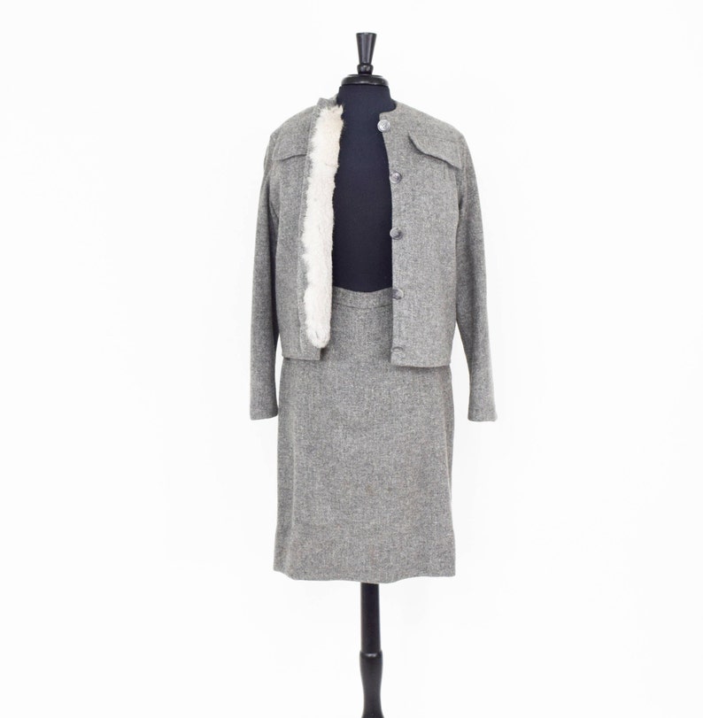 May include: A gray tweed skirt suit with a faux fur collar on the jacket. The jacket has a button closure and the skirt is knee-length.