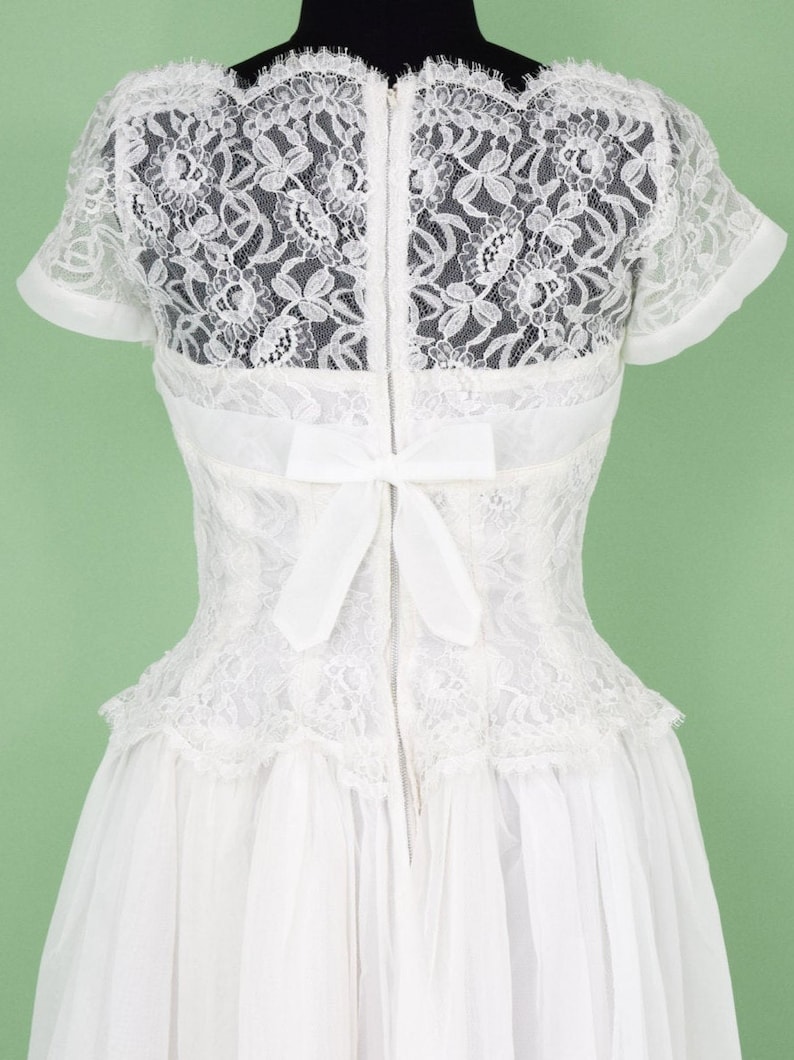 Puede incluir: Vestido de novia blanco de encaje con un lazo en la espalda y una cremallera.