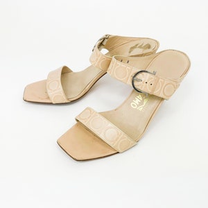 May include: A pair of beige leather heeled sandals with a buckle closure and a Salvatore Ferragamo logo on the sole.