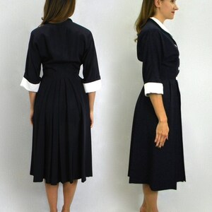 Pode incluir: Duas mulheres vestindo um vestido azul marinho com colarinho e punhos brancos. O vestido tem uma saia plissada e um corpete justo.