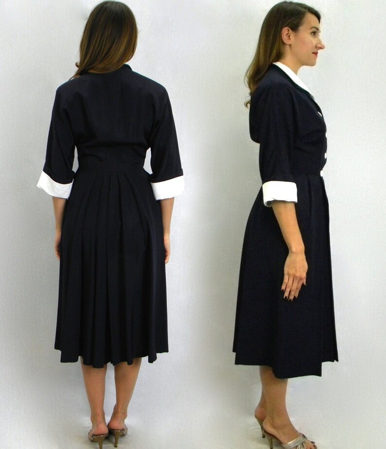 Pode incluir: Duas mulheres vestindo um vestido azul marinho com colarinho e punhos brancos. O vestido tem uma saia plissada e um corpete justo.