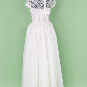 Puede incluir: Un vestido de novia blanco de encaje con un corpi&ntilde;o ajustado y una falda completa. El vestido tiene una superposici&oacute;n de encaje y un lazo en la espalda.