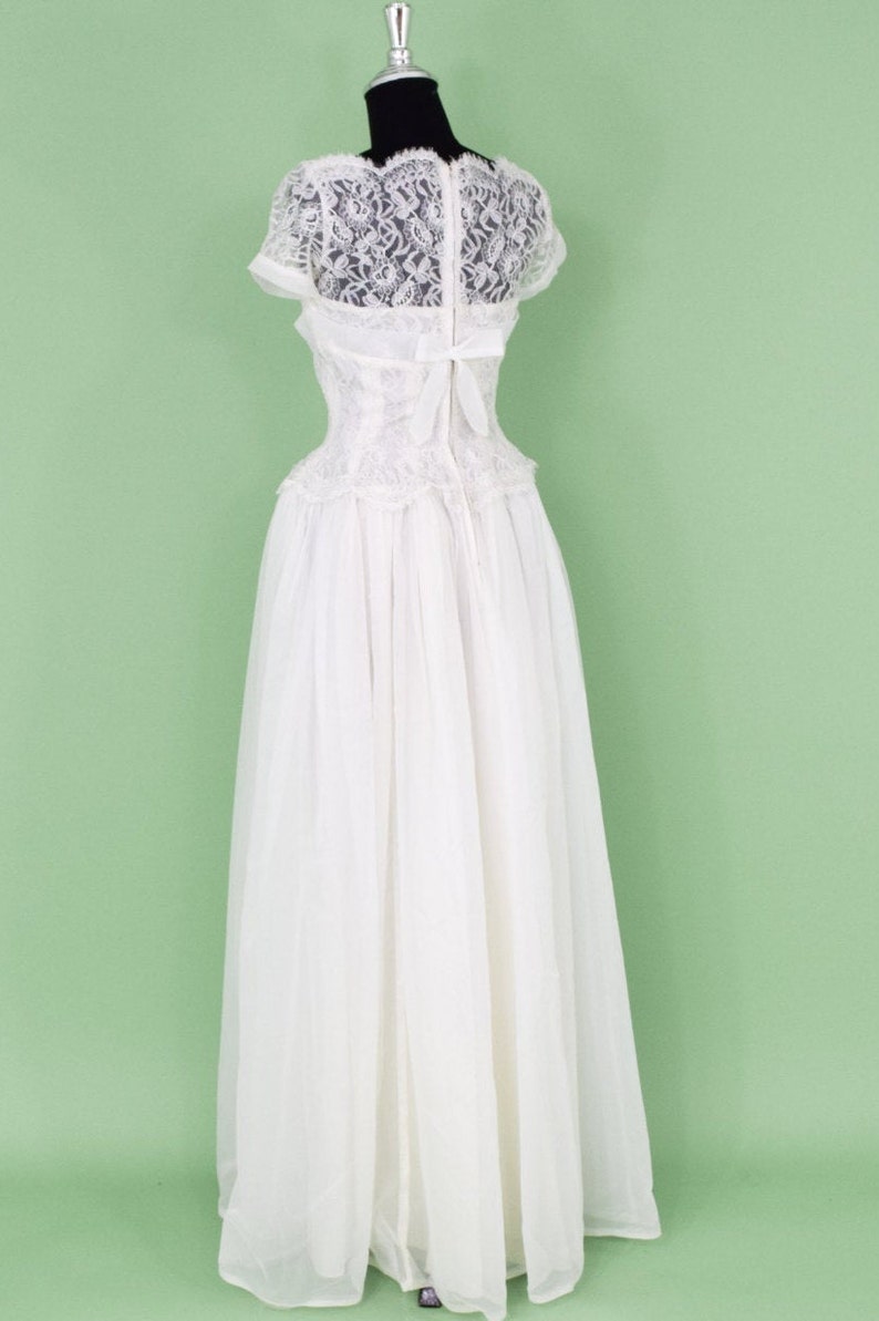 Puede incluir: Un vestido de novia blanco de encaje con un corpi&ntilde;o ajustado y una falda completa. El vestido tiene una superposici&oacute;n de encaje y un lazo en la espalda.