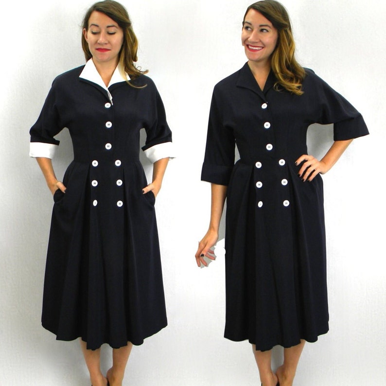 Pode incluir: Um vestido azul marinho com colarinho e punhos brancos. O vestido tem fecho de bot&otilde;es de dupla abotoadura e saia plissada.
