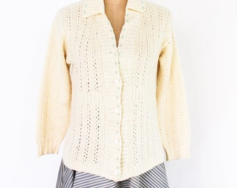 May include: A white knitted cardigan with a button-up front and a collar. The cardigan has a delicate openwork pattern and is made of a soft, lightweight yarn.