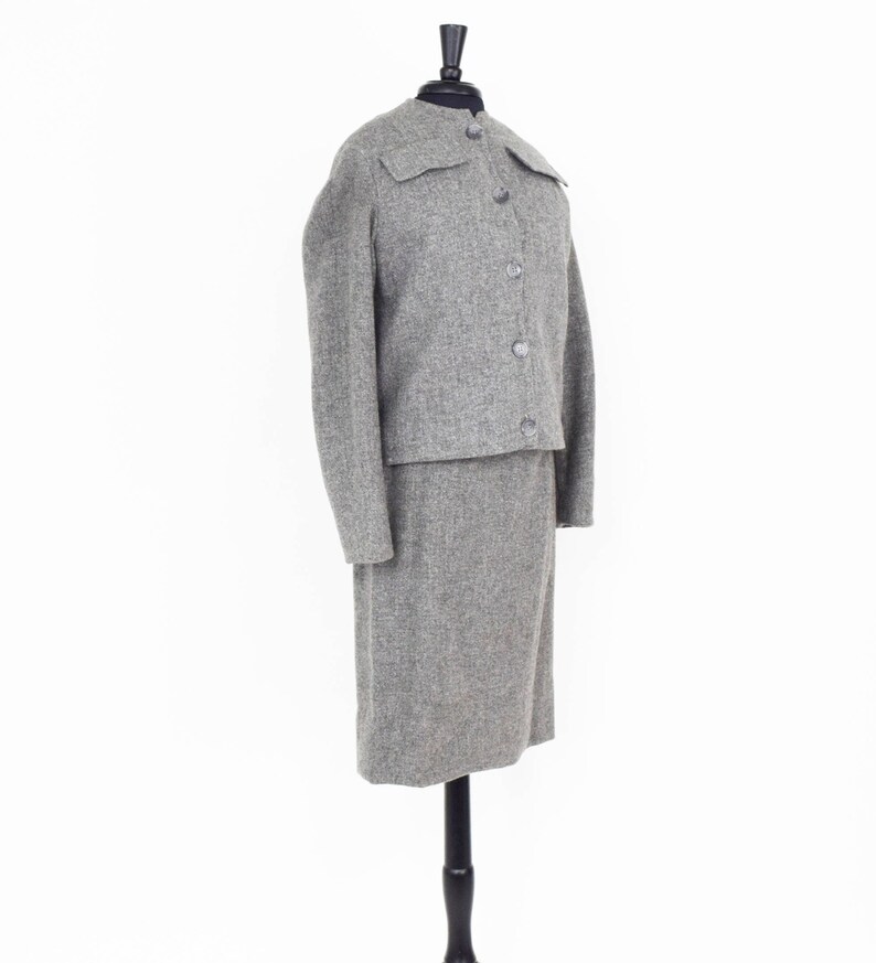 May include: A gray tweed skirt suit with a collared jacket and button closure. The jacket has a flap pocket on the chest.
