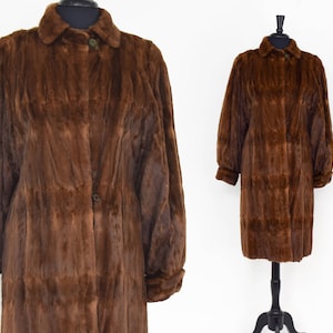 May include: A brown fur coat with a button fastening and long sleeves. The coat is on a white background.