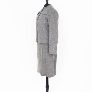 May include: A gray tweed skirt suit with a long skirt and a fitted jacket. The jacket has a mandarin collar and a single button closure.