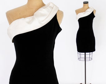 May include: A black velvet dress with a white satin one-shoulder strap. The dress is fitted and has a short length.