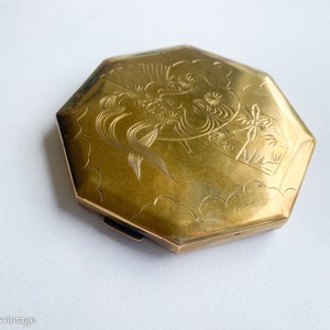 May include: A gold-toned octagonal compact with an etched design of a woman's face and flowers.