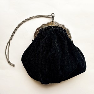 May include: A black velvet evening bag with a silver metal frame and chain strap.