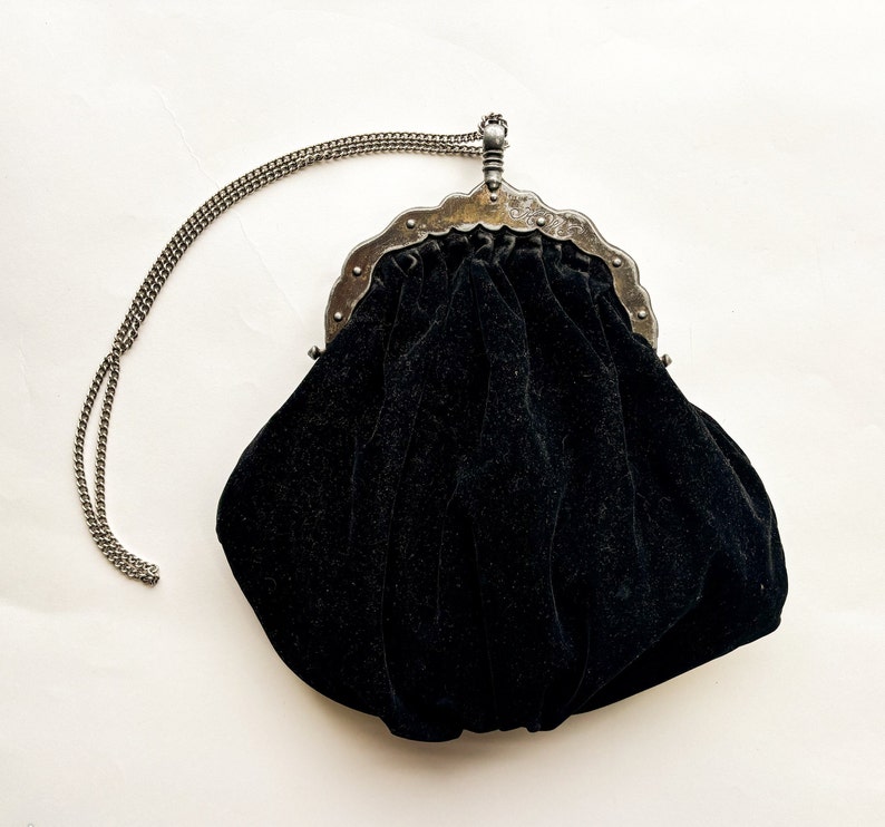 May include: A black velvet evening bag with a silver metal frame and chain strap.