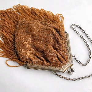 May include: A vintage beaded purse with a long silver chain. The purse is made of small brown beads and has a fringe detail. The chain is attached to the purse with a silver clasp.