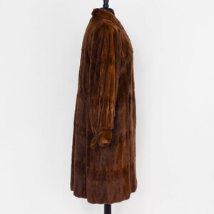 May include: A long brown fur coat with a collar and long sleeves. The coat is on a mannequin and is displayed against a white background.