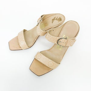 May include: A pair of beige leather heeled sandals with a buckle closure and a Salvatore Ferragamo logo pattern.