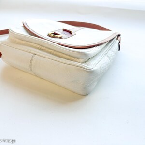Puede incluir: Bolso bandolera de cuero blanco con correa y detalles en cuero marr&oacute;n. El bolso tiene un cierre de solapa con una hebilla dorada. Estilo vintage.