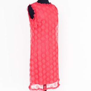 May include: A coral pink sleeveless dress with a floral pattern and a scalloped hemline. The dress is on a black mannequin.