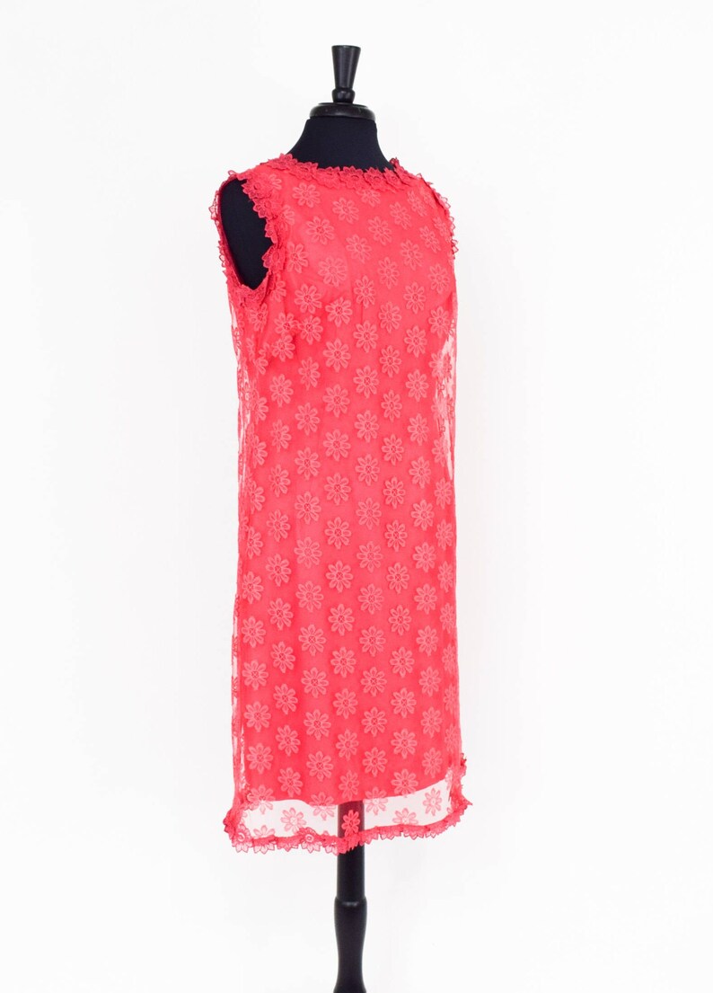 May include: A coral pink sleeveless dress with a floral pattern and a scalloped hemline. The dress is on a black mannequin.