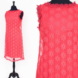 May include: A sleeveless, coral-colored dress with a floral pattern and a scalloped lace trim around the neckline and hem.