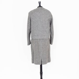 May include: A gray tweed skirt suit with a long skirt and a cropped jacket. The suit is on a mannequin.