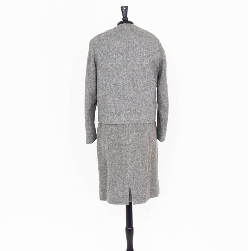 May include: A gray tweed skirt suit with a long skirt and a cropped jacket. The suit is on a mannequin.