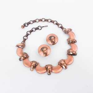 May include: A copper necklace with a chain and a series of crescent-shaped pendants. The necklace is paired with matching copper earrings.