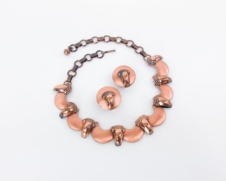 May include: A copper necklace with a chain and a series of crescent-shaped pendants. The necklace is paired with matching copper earrings.