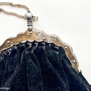 May include: A vintage black velvet purse with a silver metal frame and chain. The frame has an ornate design and the initials "M.W." are engraved on the front.