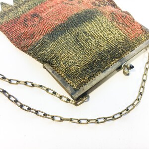 K&ouml;nnte beinhalten: Eine Vintage-Mesh-Handtasche mit einer Kettenkette. Die Tasche ist aus feinem Metallgewebe gefertigt und hat eine rot-schwarz-goldene Farbgebung.